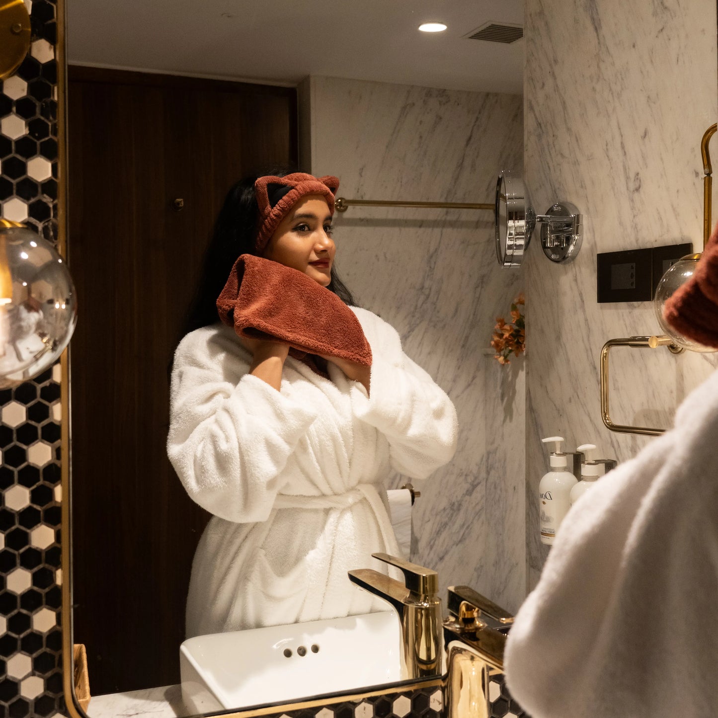 Woman using sage dark brown Kitty Bloom combo set in a bathroom mirror scene.