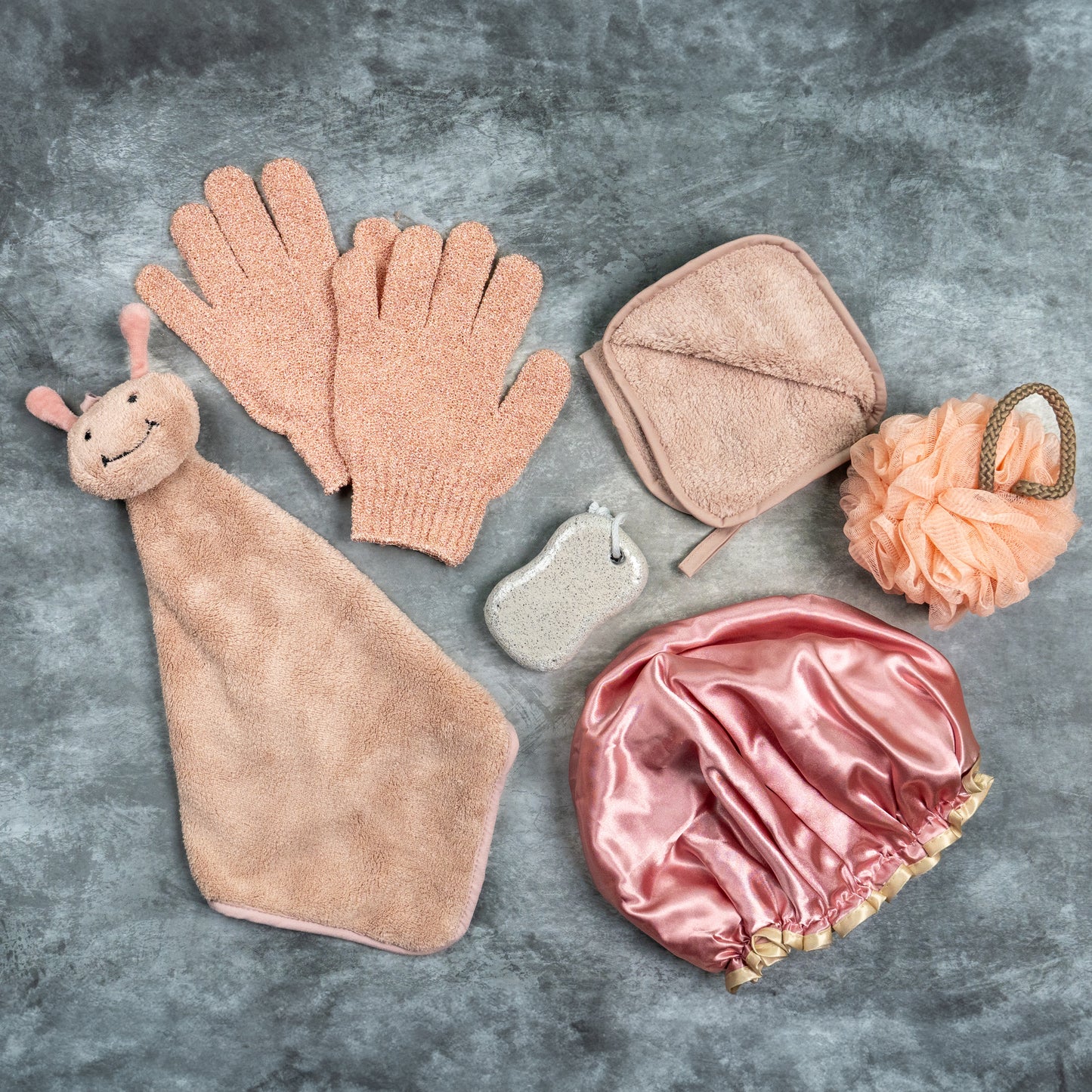 Peach-toned Luxe Bloom gloves displayed with pumice, loofah, and wooden brush