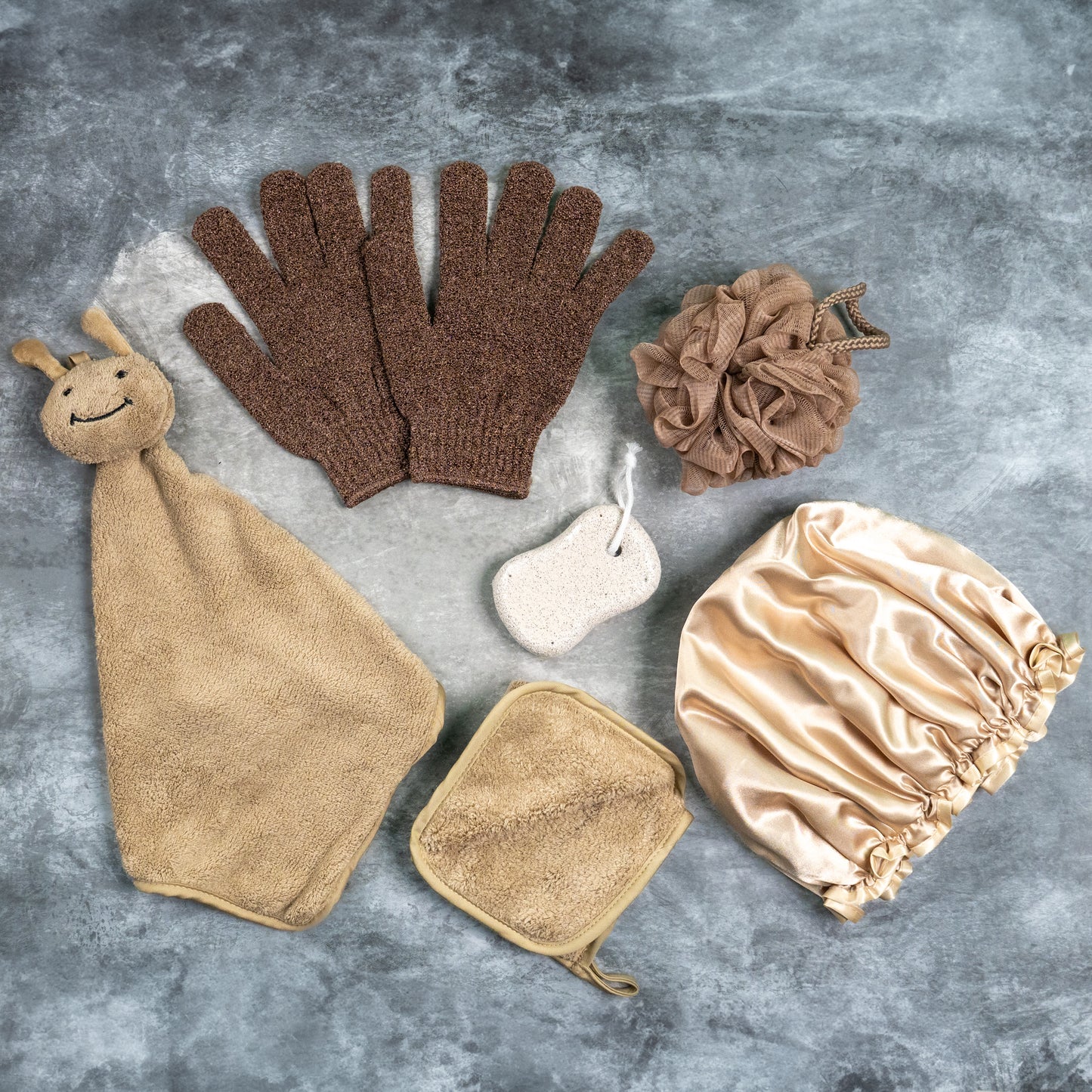 Flat lay of light brown Luxe Bloom bath gloves with pumice stone, loofah, and brush