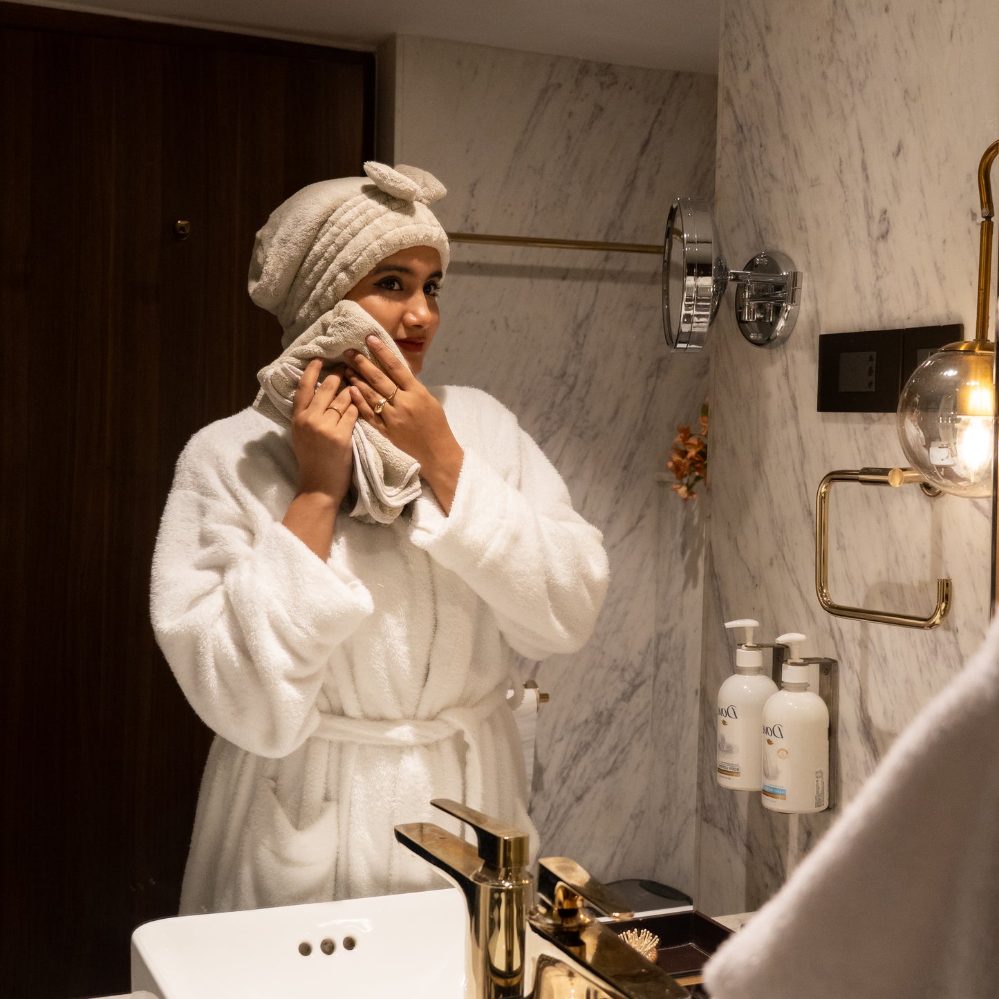 Woman enjoying a spa moment with beige Soothe Luxe towel and bow headband in a modern bathroom