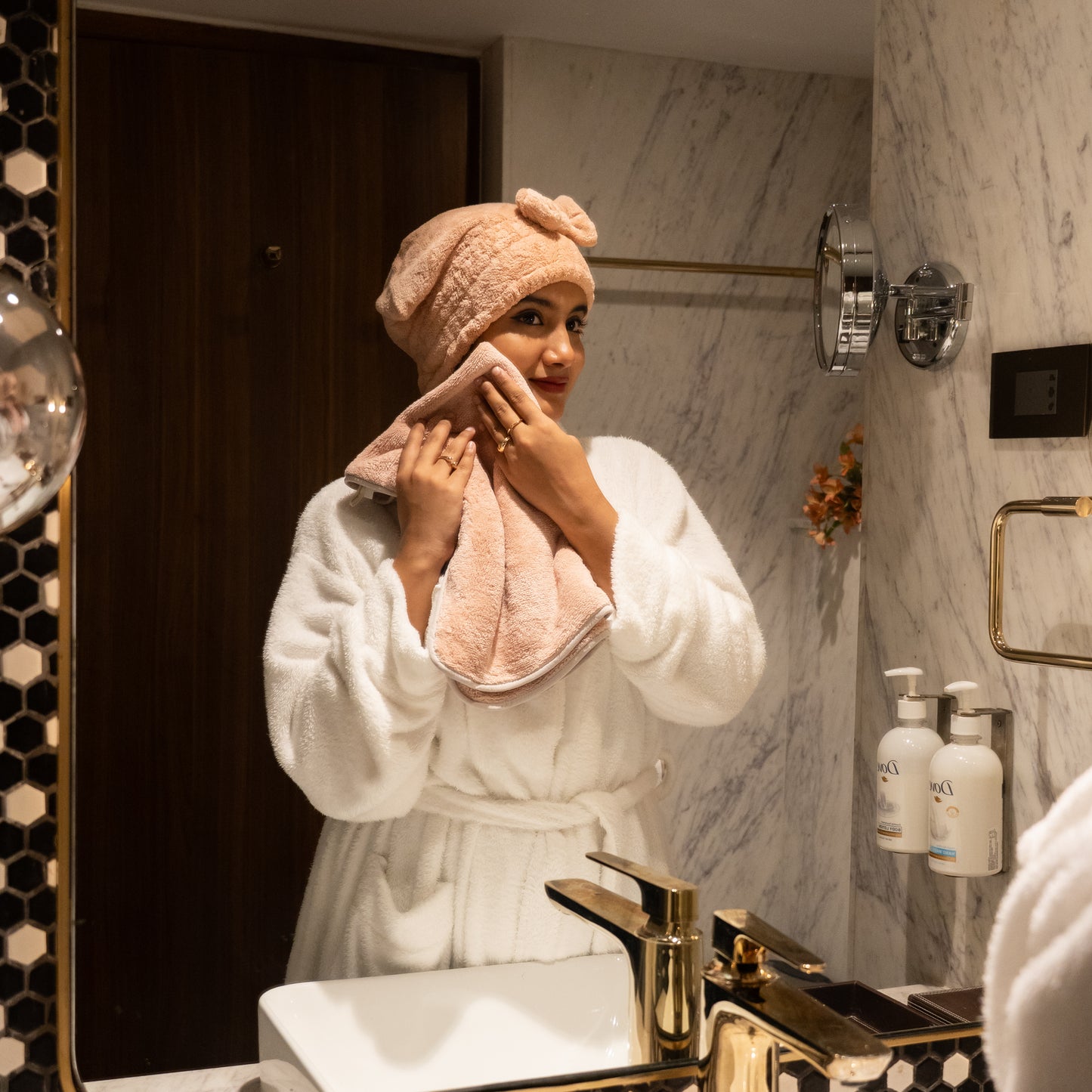 Woman enjoying a spa moment with pink Soothe Luxe towel and bow headband in a modern bathroom