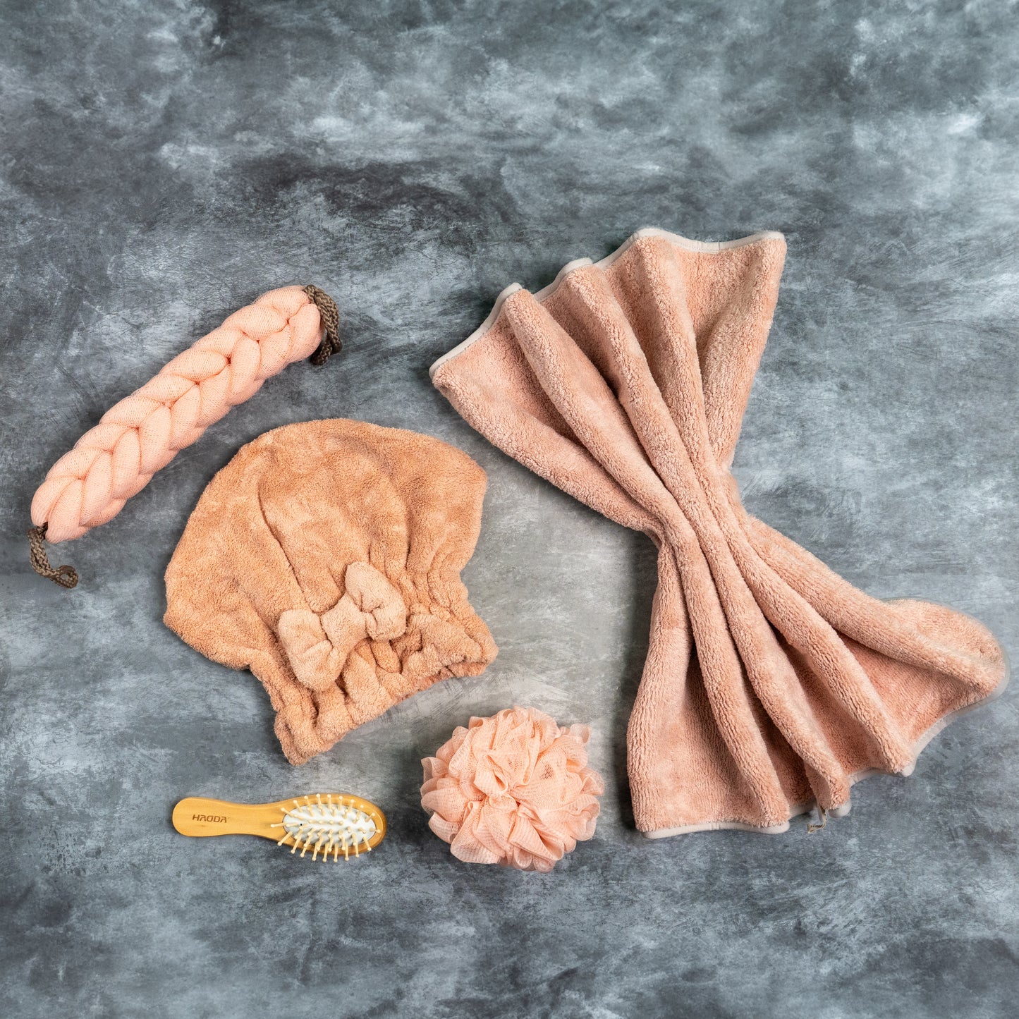 Top-down view of pink Soothe Luxe bath accessories including plush towel, braided scrubber, and exfoliating puff
