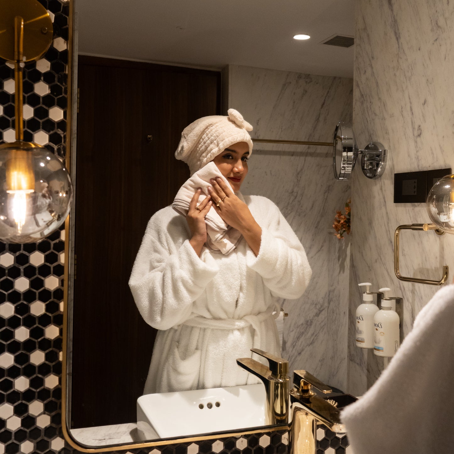 Woman enjoying a spa moment with beige Soothe Luxe towel and bow headband in a modern bathroom