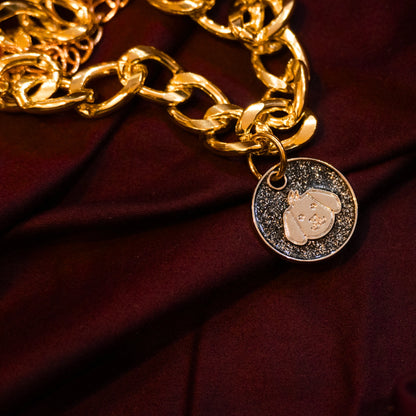 Gold pet necklace with black glitter dog-face charm displayed on a maroon cloth background