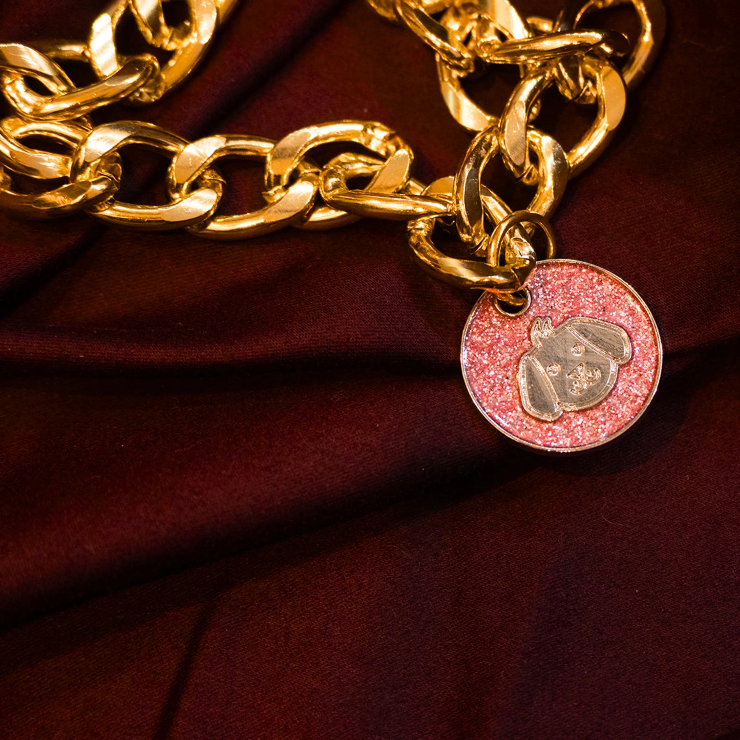 Gold pet necklace with white glitter dog-face charm displayed on a maroon cloth background