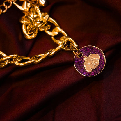 Gold pet necklace with purple glitter dog-face charm displayed on a maroon cloth background
