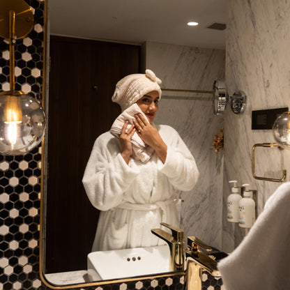 Woman enjoying a spa moment with beige Soothe Luxe towel and bow headband in a modern bathroom
